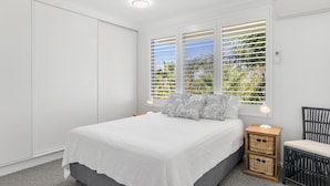 A bedroom with a bed, a nightstand, a chair, and a window with blinds. - Byron Breeze 7 ~ Luxury Penthouse 3 Bedroom Apartment (Byron Bay)