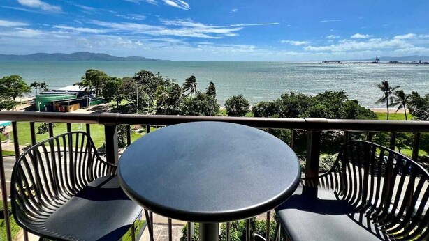 A balcony with a table and chairs overlooking a coastal view with mountains in the distance. - It's all about the views! (Townsville City)