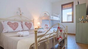 Una cama bien hecha con almohadas con forma de corazón, una lámpara de noche y una cama individual al fondo.