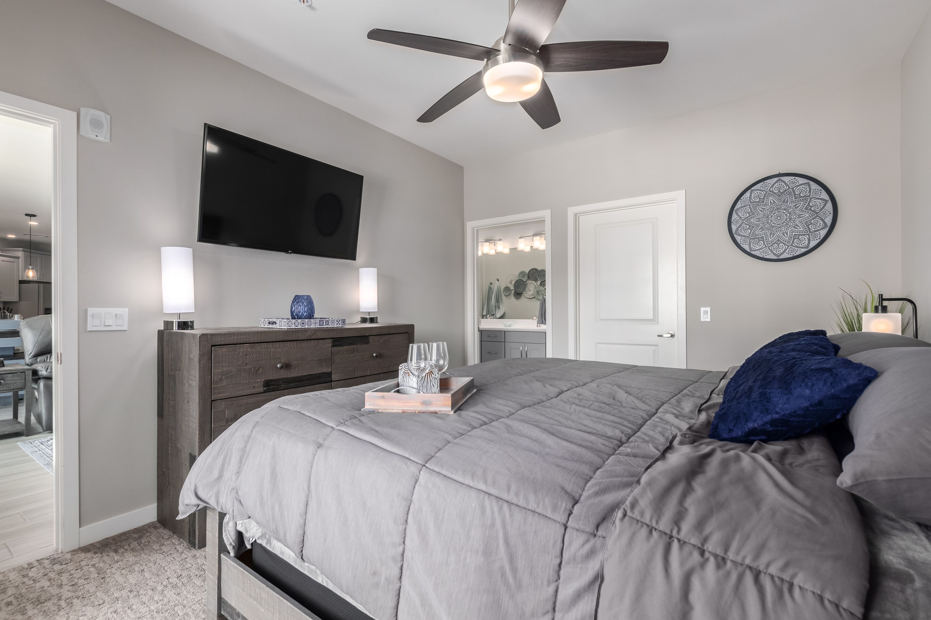 A bedroom with a bed, a ceiling fan, a TV, a dresser, and a mirror.