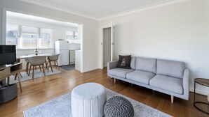 A modern living room with a grey sofa, a TV, and a dining area with a table and chairs. - Bach on Pitau - Mt Maunganui Holiday Home (Mt Maunganui)