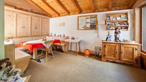 A cozy room with wooden beams, a dining table, a bench, a small table with a vase, and a cabinet with decorative items. - Vacation Apartment "Moosmair 2" with Mountain View, Wi-Fi, Balcony & Garden (St. Martin in Passeier)