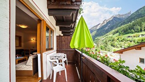 A balcony with a wooden railing, a table with chairs, and a green umbrella. - Vacation Apartment "Moosmair 2" with Mountain View, Wi-Fi, Balcony & Garden (St. Martin in Passeier)
