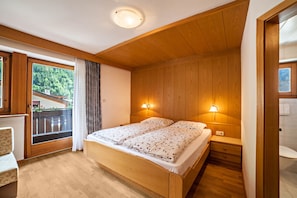 Un dormitorio con cama de madera, dos lámparas de noche, una ventana con vistas a la vegetación y un balcón.