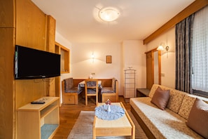 Una sala de estar con televisor de pantalla plana, muebles de madera, un sofá y un comedor con sillas y una mesa.
