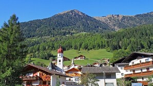 A mountain village with traditional wooden houses, a church with a bell tower, and a clear view of the surrounding hills. - Vacation Apartment "Moosmair 2" with Mountain View, Wi-Fi, Balcony & Garden (St. Martin in Passeier)