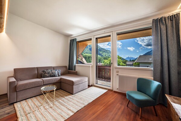 Un salon moderne comprenant un canapé, un fauteuil, une petite table et offrant une vue sur un paysage montagneux grâce à de grandes fenêtres.