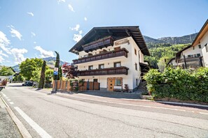 Un immeuble à plusieurs étages doté de balcons, une enseigne indiquant qu’il s’agit d’un hôtel, et une vue sur les montagnes en arrière-plan.