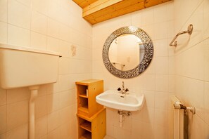Une salle de bain comprenant des toilettes, un lavabo, une étagère en bois et un miroir décoratif.