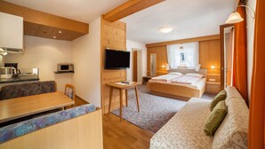 Een kamer met houten plafond, een bed met hoofdeinde, een televisie, een tafeltje, een bank en een raam met gordijnen.