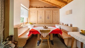 Een eetgedeelte met een houten tafel, bankjes en een hoge plafond met zichtbare balken.