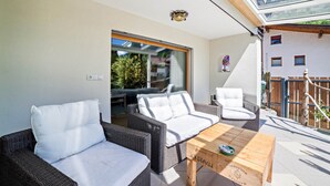 Een balkon met rieten meubilair, een houten tafel en uitzicht op de omgeving.