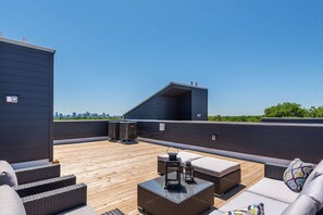 A rooftop terrace with outdoor furniture, a city skyline view, and a modern building structure.