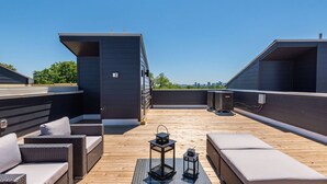 Eine Dachterrasse mit Gartenmöbeln, zwei schwarzen Laternen und einer großen Klimaanlage.