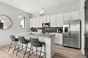A modern kitchen with white cabinets, a stainless steel refrigerator, a microwave, and a granite island with bar stools.