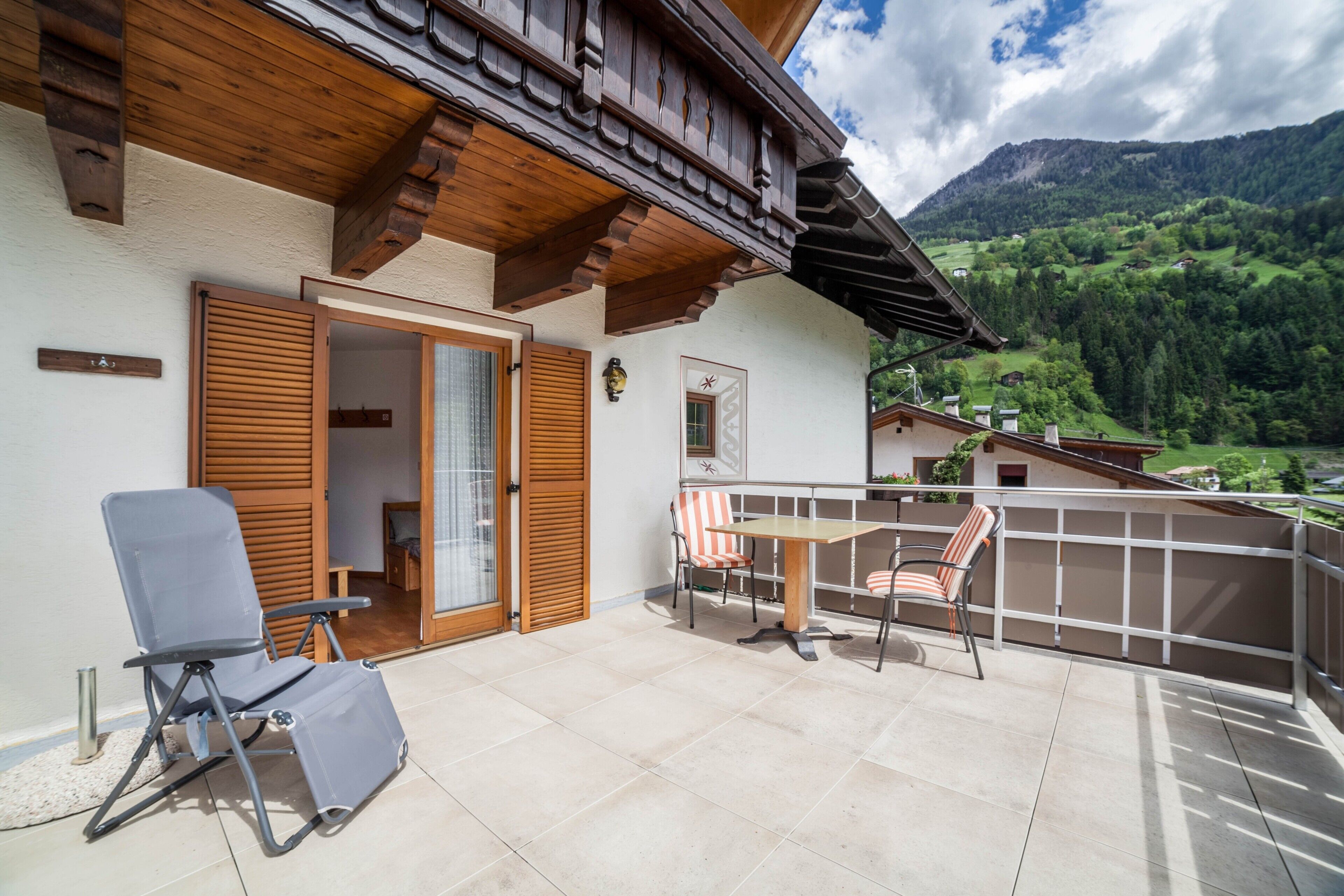 Ein Balkon mit Tisch und Stühlen, einer Holzbalkendecke und Blick auf ein grünes Tal.