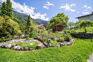 A garden with a gazebo, a stone wall, and a mountain backdrop. - Vacation Apartment "Moosmair 3" with Mountain View, Wi-Fi, Balcony & Garden (St. Martin in Passeier)