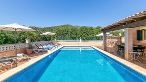 A swimming pool with lounge chairs and umbrellas, surrounded by a stone wall and greenery. - Villa Bonavista with Mountain View, Private Pool, Wi-Fi, Terrace & Garden (Capdepera)