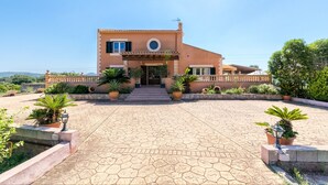 A two-story house with a tiled patio, potted plants, and a clear sky. - Villa Bonavista with Mountain View, Private Pool, Wi-Fi, Terrace & Garden (Capdepera)