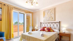 A bedroom with a bed, two bedside tables, a chandelier, a painting, and a sliding glass door leading to an outdoor area. - Villa Bonavista with Mountain View, Private Pool, Wi-Fi, Terrace & Garden (Capdepera)