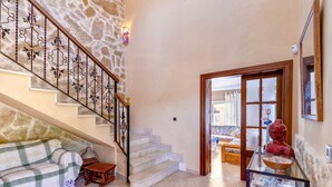A staircase with ornate metal railings, a stone wall, a sofa, and a glass display case with decorative items. - Villa Bonavista with Mountain View, Private Pool, Wi-Fi, Terrace & Garden (Capdepera)