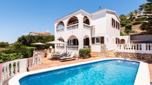 Une villa blanche à deux étages, dotée d’une piscine, d’un espace salon extérieur et d’un escalier en pierre.