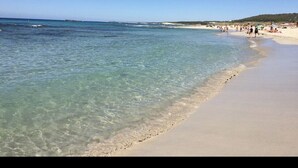Une plage à l’eau claire, avec un rivage sablonneux et des personnes visibles au loin.