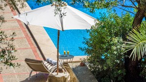 Et poolområde med hvid parasol, to liggestole, et bord med drikkevarer og en potteplante.