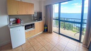 Et kompakt køkken med køleskab, mikroovn og elkedel. Der er en stor skydedør, der fører ud til en balkon med havudsigt.