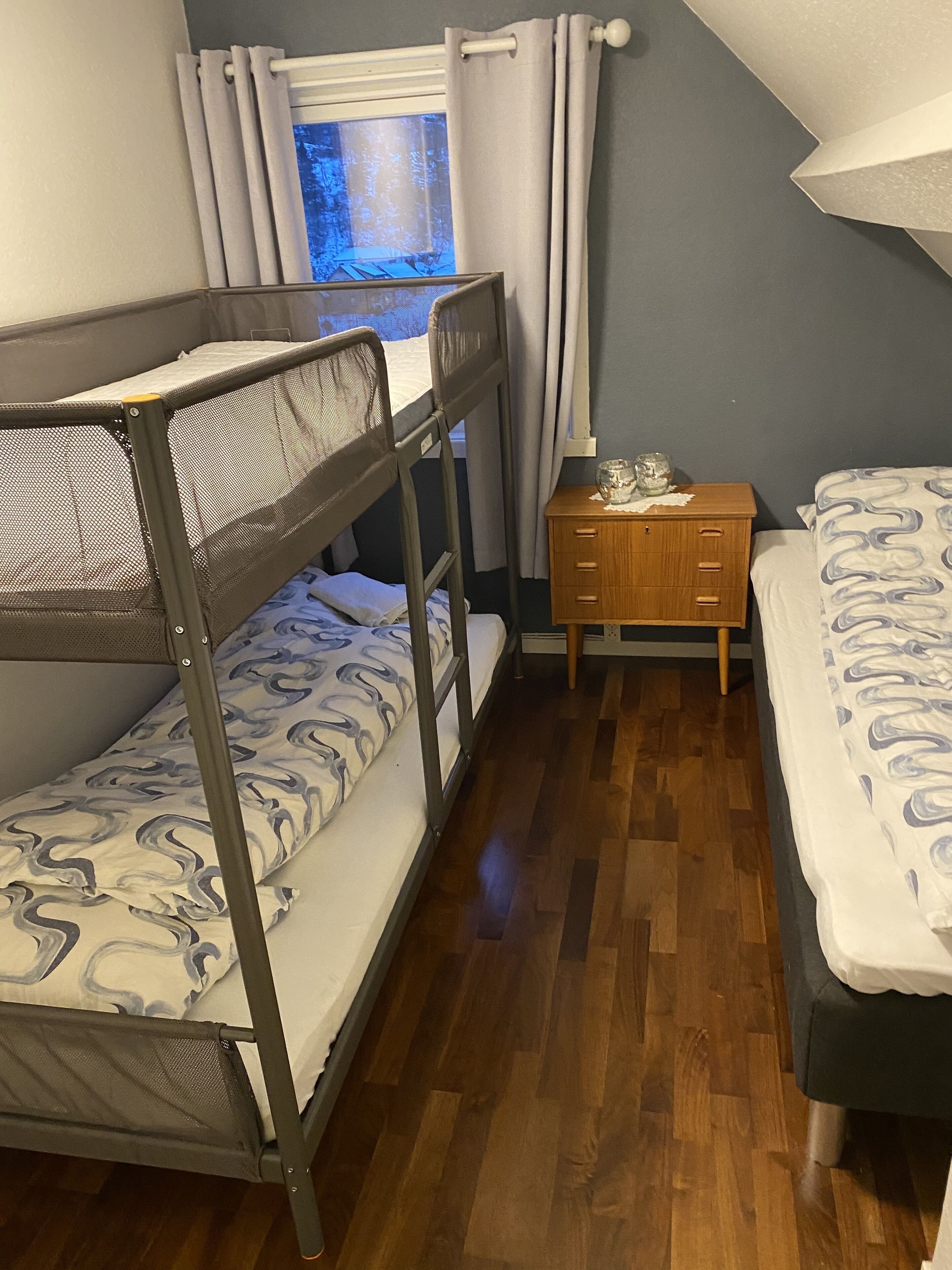 A bunk bed room with a wooden nightstand and a window with curtains.