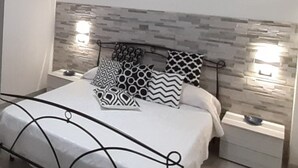 Un dormitorio moderno con cama, almohadones estampados, una mesita de noche y una lámpara colgante.
