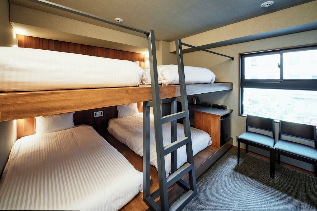 A bunk bed room with a ladder, a desk, and a window.
