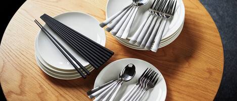 Une table ronde en bois, sur laquelle sont disposées trois assiettes blanches, chacune accompagnée d’une paire de baguettes, d’une cuillère et d’une fourchette.