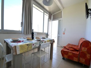 Zona pranzo con tavolo apparecchiato per due, divano e finestra con tende.