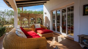 A covered outdoor seating area with wicker furniture, a decorative wooden structure, and a sliding glass door leading to an interior space. - Villa "Luna" with Sea Views, Pool, Air Conditioning, Terraces & Garden (Cala d'Or)