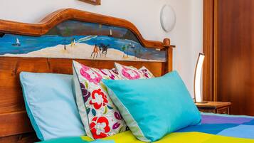 Una cama con ropa de cama y almohadas coloridas, un cabecero de madera con un dibujo pintado de playa y una mesita de noche con una lámpara.
