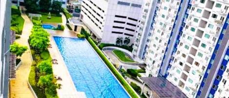 A high-rise residential building with a swimming pool, surrounded by greenery and other buildings.