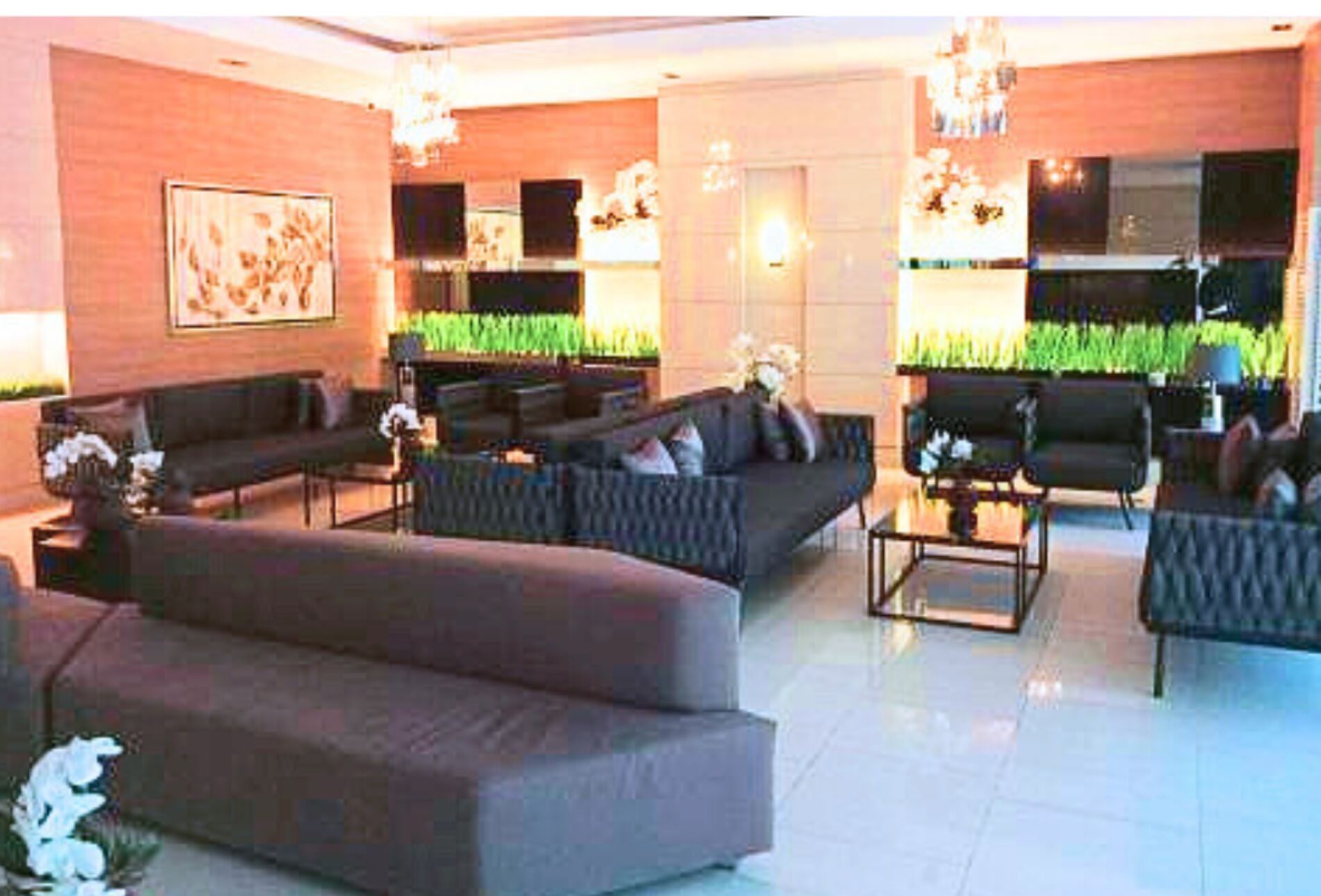Un vaste espace de vie comprenant un grand canapé, un canapé plus petit et une table basse. On y trouve deux tables d’appoint ornées d’objets décoratifs. La pièce présente un design moderne, avec un grand tableau au mur et un lustre.