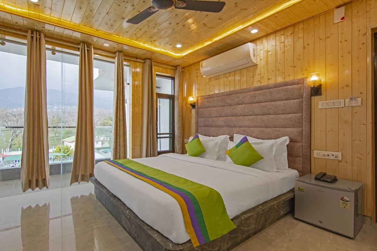 A hotel room with a large bed, wooden walls, a ceiling fan, and a view of the mountains.
