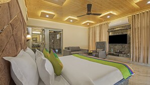 Une chambre d’hôtel avec un lit, un canapé, une télévision et une salle de bain visible à travers une porte en verre.