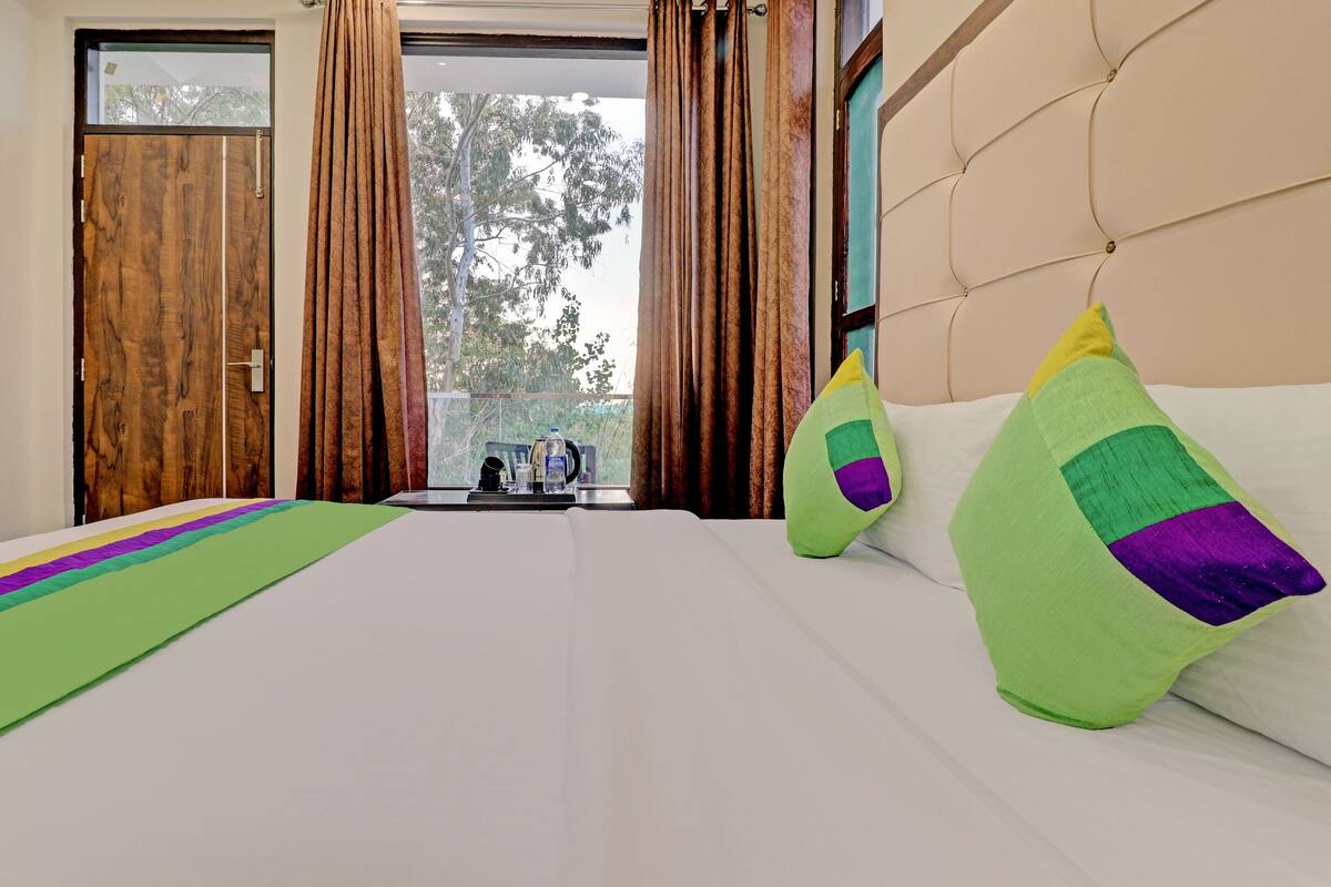 A hotel room with a large bed, a view of trees through the window, and a wooden door.