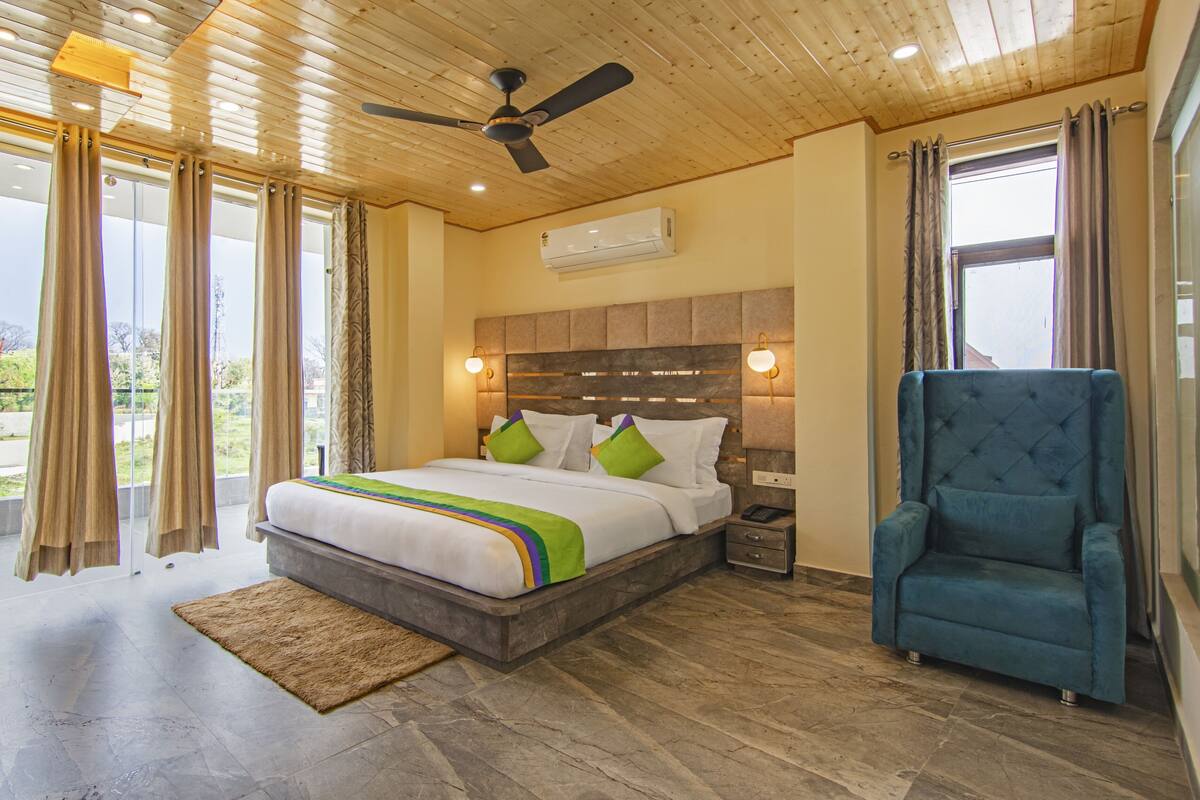 A bedroom with a large bed, a nightstand, a blue armchair, and a ceiling fan.