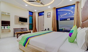 Ein Hotelzimmer mit einem großen Bett, einem Fernseher, einem Schreibtisch und einem Fenster mit Blick.