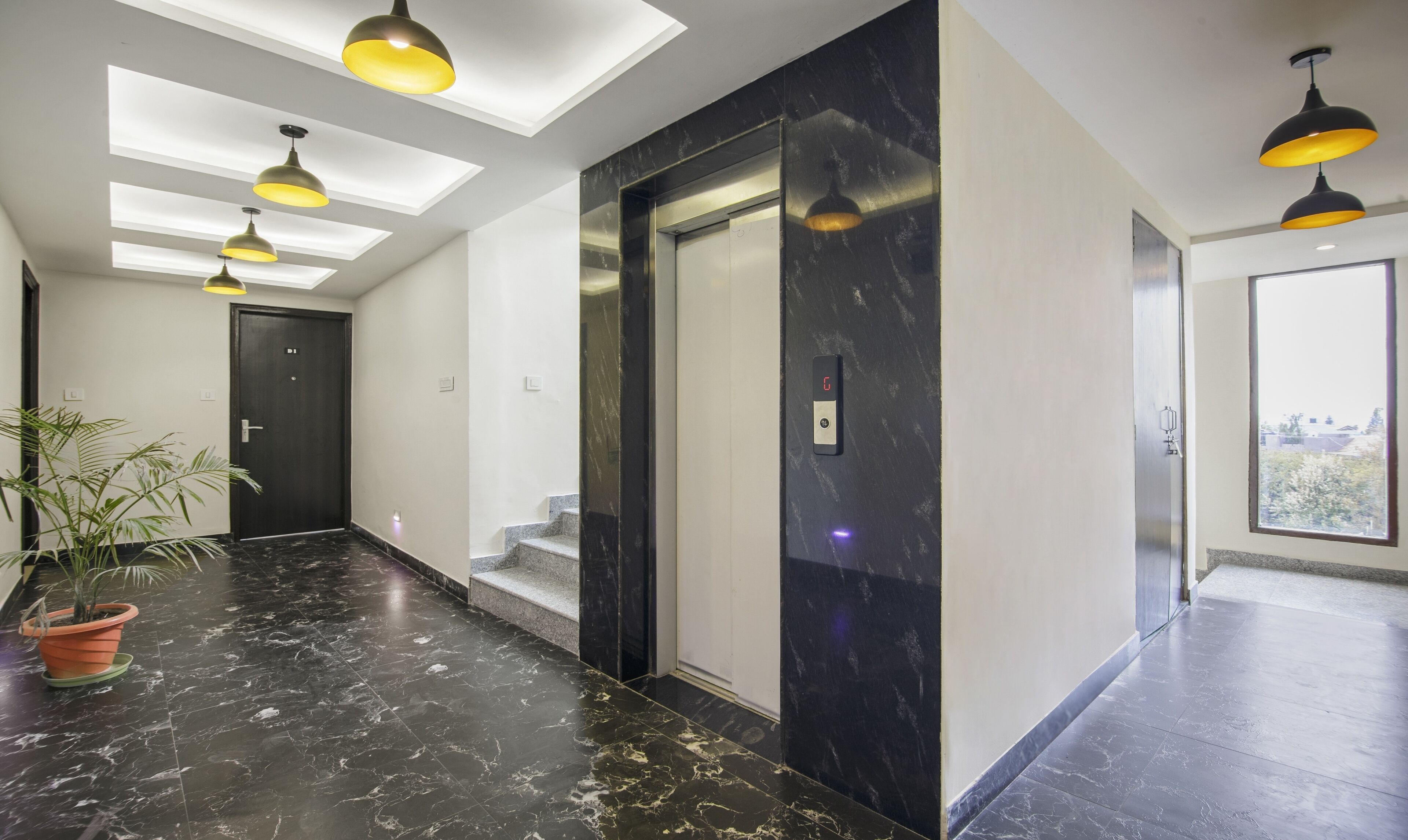Um elevador moderno com painel digital, piso de mármore e iluminação pendente.