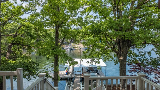 A wooden deck with a staircase leading to a dock area with boats and a covered seating area.