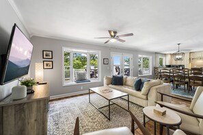 A spacious living room with a large TV, comfortable seating, a ceiling fan, and a view of the outdoors. - Lakatude Adjustment - Lakefront w/Dock & Kid's Zone (Lake Ozark)