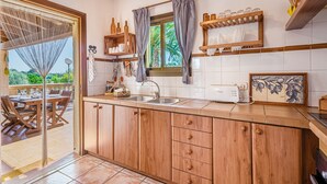 A kitchen with wooden cabinets, a sink, and a window with curtains. - Vacation Home Es Garballons with Garden, Wi-Fi, Pool & Terrace (Manacor)