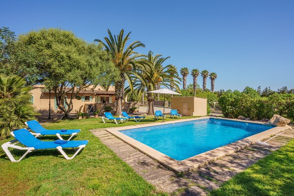 Une piscine avec des chaises longues, des palmiers et un bâtiment en arrière-plan.