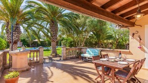 An outdoor patio with a wooden table and chairs, a stone bench, and a pool in the background. - Vacation Home Es Garballons with Garden, Wi-Fi, Pool & Terrace (Manacor)