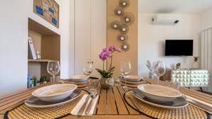 Una mesa de comedor dispuesta con platos, cubiertos y vasos, una orquídea en maceta y un panel decorativo en la pared.